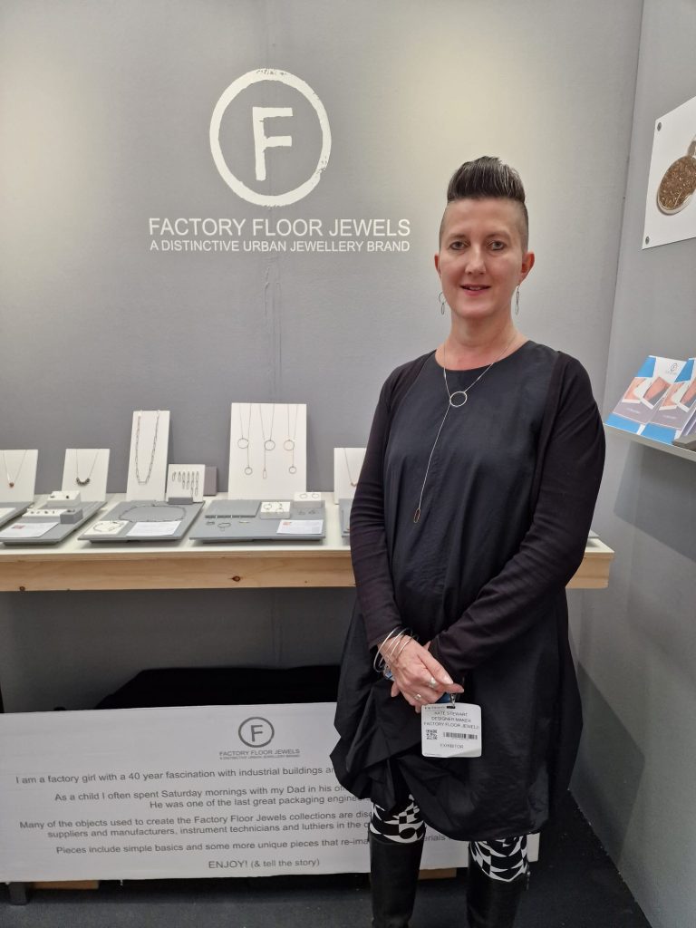 Kate owner of ACID member Factory Floor Jewels standing next to jewellery design exhibition at Top Drawer