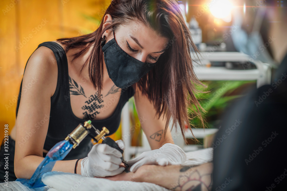 Using for image to depict article about Kat Von D copyright judgment. Image copyright of  Adobe Stock. Image of a female tattooist mid tattoo, looking down holding the tattoo gun on a customers arm. 