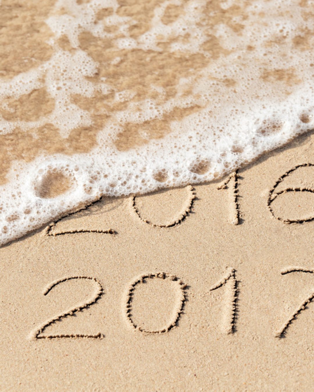 2016 2017 inscription written on wet yellow beach sand being washed by sea wave